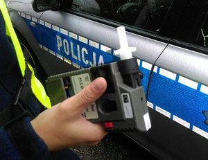 Zbliżenie ręki trzymającej alkotest na tle radiowozu