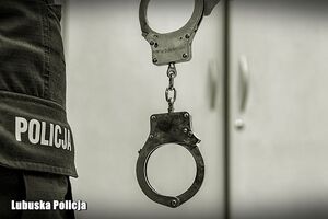 Zbliżenie kajdanek zwisających w ręce policjanta wzdłuż spodni