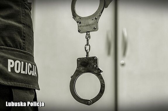 Zbliżenie kajdanek zwisających w ręce policjanta wzdłuż spodni