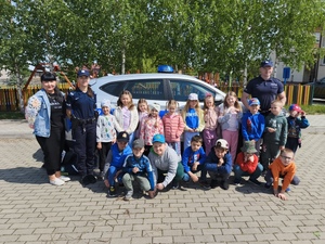 Na podwórku szkoły dwójka policjantów pozująca z grupą dzieci do zdjęcia na tle radiowozu