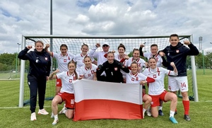 W bramce drużyna kobiet ubrana w biało-czerwone stroje piłkarskie trzymająca flagę Polski