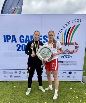 Dwie kobiety ubrane na sportowo trzymające w rękach trofea sportowe
