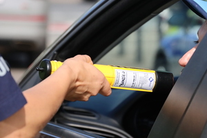 Zbliżenie ręki policjanta trzymającej alkotest i osoby wewnątrz pojazdu poddającej się badaniu