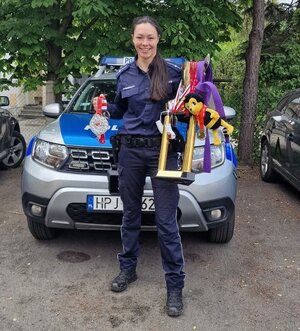 Uśmiechnięta policjantka trzymająca w rękach medale i trofea sportowe na tle radiowozu
