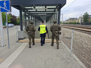 Widziani od tyłu wchodzący do przejścia podziemnego na peronie policjant i dwaj żołnierze