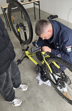Policjant znakujący wewnątrz pomieszczenia rower odwrócony do góry kołami