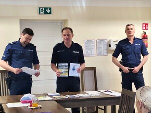 Trzech policjantów stojących za stołami, na których leżą ulotki