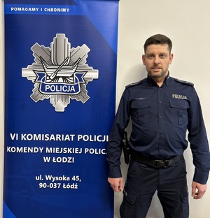 Zdjęcie policjanta obok banneru VI Komisariatu Policji w Łodzi