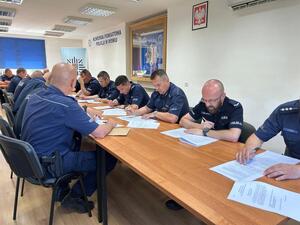 Kilkunastu policjantów przy stole rozwiązujących test