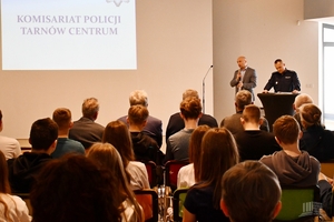 Spotkanie w sali konferencyjnej, przy mównicy policjant oraz mężczyzna w marynarce