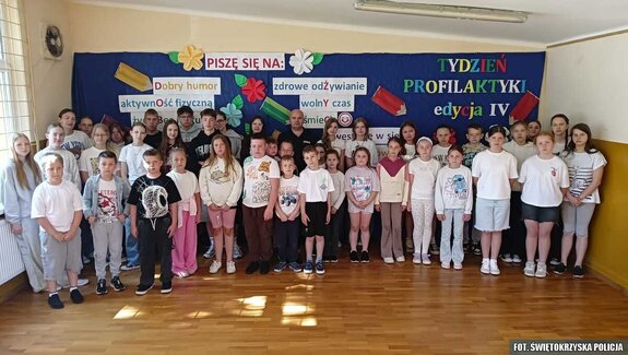 Dzieci pozujące do zdjęcia z policjantem w sali gimnastycznej
