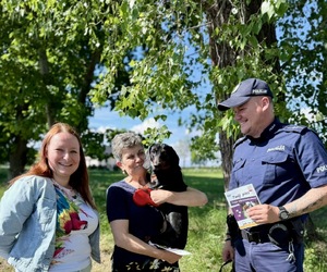 Na tle zieleni dwie kobiety z psem na rękach rozmawiające z policjantem