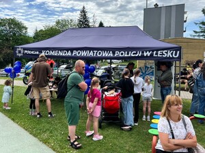 Piknik na tle zieleni widoczny namiot wystawienniczy Komendy Powiatowej Policji w Lesku obok tłum opiekunów z dziećmi