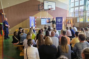 Na sali gimnastycznej mężczyzna prowadzący wykład, obok policjant, sala wypełniona młodzieżą