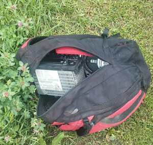 Leżąca na trawie torba wewnątrz, której widoczne jest radio samochodowe