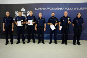Grupa policjantów z dyplomami i pucharami stojąca na tle ścianki Komendy Wojewódzkiej Policji w Lublinie