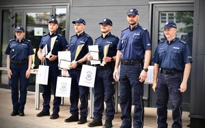 Na tle budynku komisariatu grupa policjantów z dyplomami i pucharami