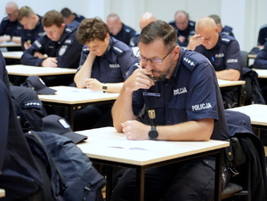 Grupa policjantów przy stolikach pochylona nad rozwiązywaniem testu wiedzy