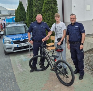 Dwaj policjanci a pomiędzy nimi młody chłopak z rowerem
