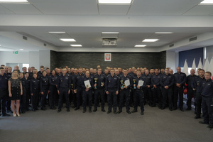 Duża grupa policjantów pozująca wewnątrz sali do zdjęcia. Część z nich w rękach trzyma puchary sportowe i dyplomy