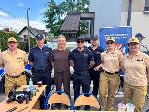 Grupa policjantów i strażaków pozująca do zdjęcia przy stoisku ekspozycyjnym ze sprzętem policyjnym