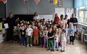Dwójka policjantów, wychowawczynie oraz duża grupa przedszkolaków pozująca do zdjęcia wewnątrz sali