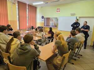 Dwóch policjantów podczas prelekcji dla młodzieży szkolnej wewnątrz sali lekcyjnej