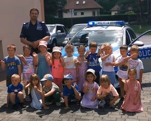 Dzieci wraz z policjantem pozujące do zdjęcia na tle budynku i radiowozu