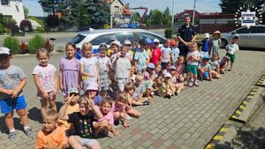 Duża grupa dzieci wraz z policjantem pozująca na ulicy do zdjęcia na tle radiowozu