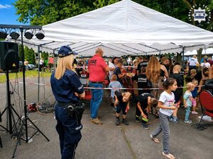 Piknik pod namiotami wystawienniczymi, na pierwszym planie widziana z tyłu policjantka