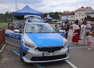 Piknik na placu, widoczne namioty wystawiennicze rodziców z dziećmi, na pierwszym planie radiowóz
