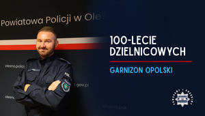 Uśmiechnięty policjant na tle ścianki KPP w Oleśnie i napis 100. lecie dzielnicowych