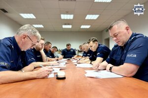 Policjanci siedzący wzdłuż stołu konferencyjnego rozwiązujący test