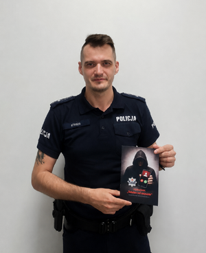 Policjant trzymający w ręku ciemną książeczkę z napisem poradnik