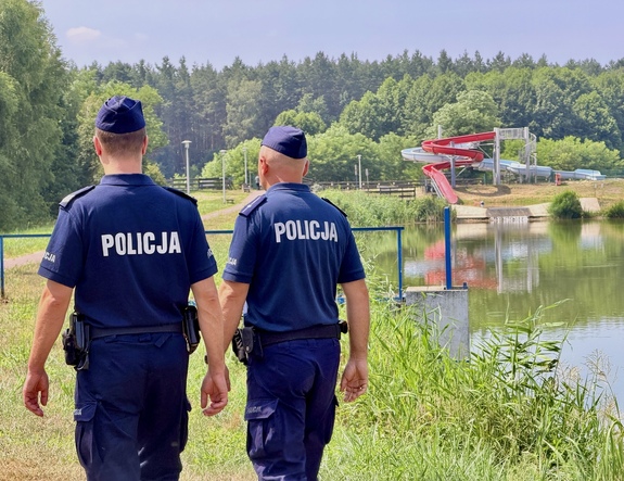 Widziani z tyłu dwaj policjanci nad brzegiem akwenu.