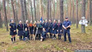 Na tle lasu pozująca do zdjęcia grupa harcerek oraz policjant