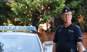 Policjant w dojrzałym wieku obok radiowozu na tle zieleni