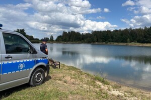 Policjant stojący przy radiowozie typu bus nad brzegiem zbiornika wodnego