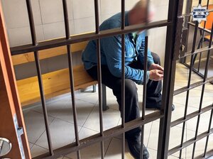 Mężczyzna siedzący na drewnianej ławce za kratami