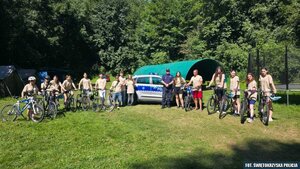 Na skraju leśnej polany policjant oraz grupa młodzieży z rowerami pozująca do zdjęcia