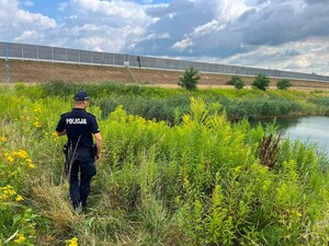 Widziany z tyłu policjant na brzegu porośniętego zielenią zbiornika wodnego