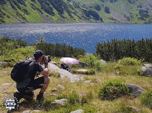 Widziany z tyłu mężczyzna z aparatem fotograficznym na skraju górskiego jeziora