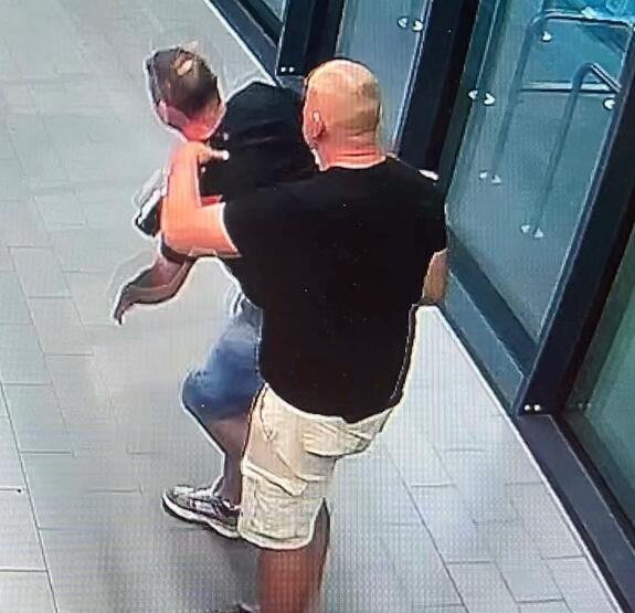 Zdjęcie z kamery przemysłowej: mężczyzna po cywilnemu chwytający drugiego mężczyznę