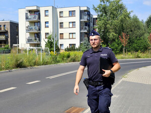 Policjant z teczką biurową idący chodnikiem wzdłuż osiedla
