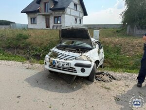 Rozbity w rowie biały samochód osobowy na tle budynku w budowie