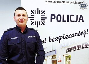 Policjant na tle rozmytej sylwetki budynku komisariatu