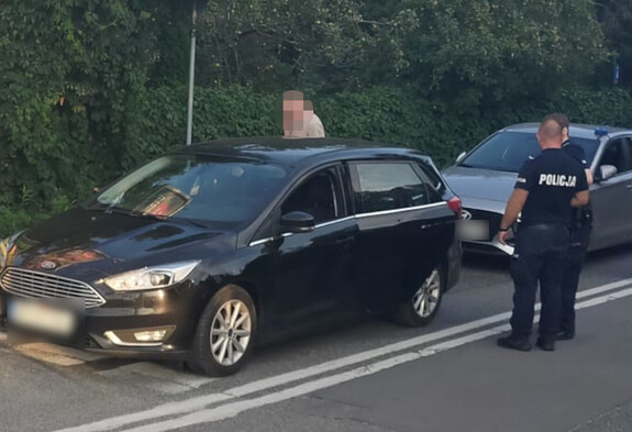 Widziany z góry policjant obok mężczyzny stojącego przy czarnym samochodzie kombi