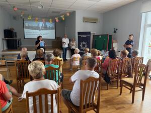 Dwójka policjantów oraz dwójka osób po cywilnemu prowadzących pogadankę dla zgromadzonych w sali seniorów
