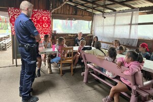 policjant w mundurze stoi przed grodzką dzieci siedzących przy stolikach