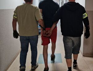 dwóch policjantów prowadzi mężczyznę z założonymi na rękach kajdankami